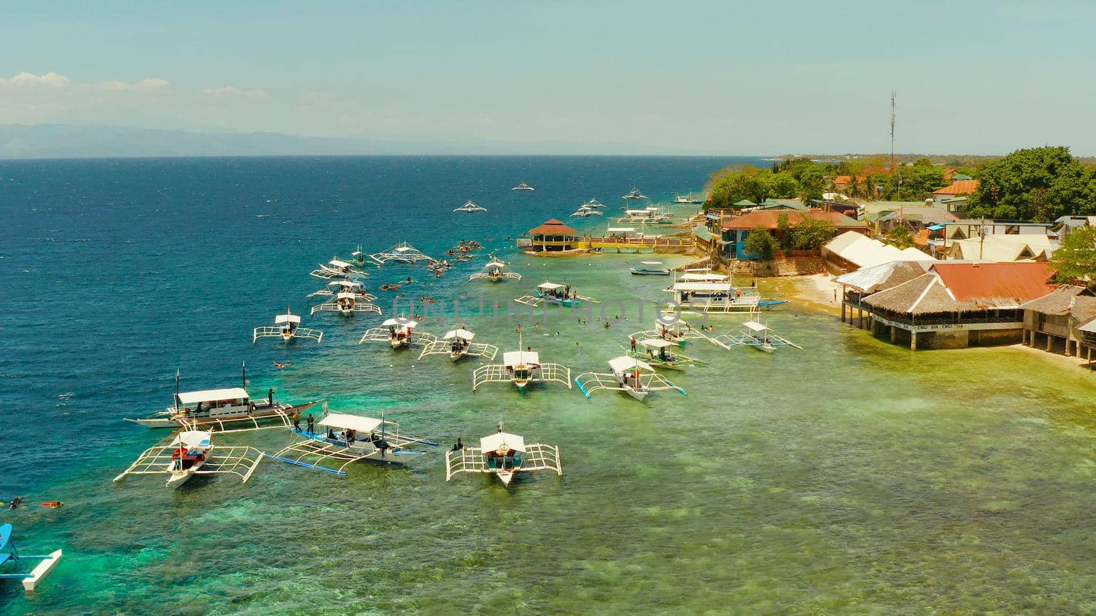 Tourists snorkeling over coral reef with clear blue ocean water, aerial view. Moalboal, Philippines. People swim in the transparent sea between coral reefs. Summer and travel vacation concept.