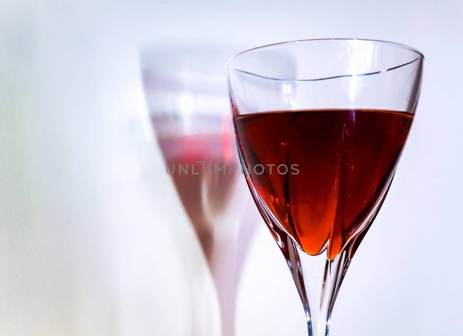 Tall wine glass filled with red wine near white wall with colorful shadow