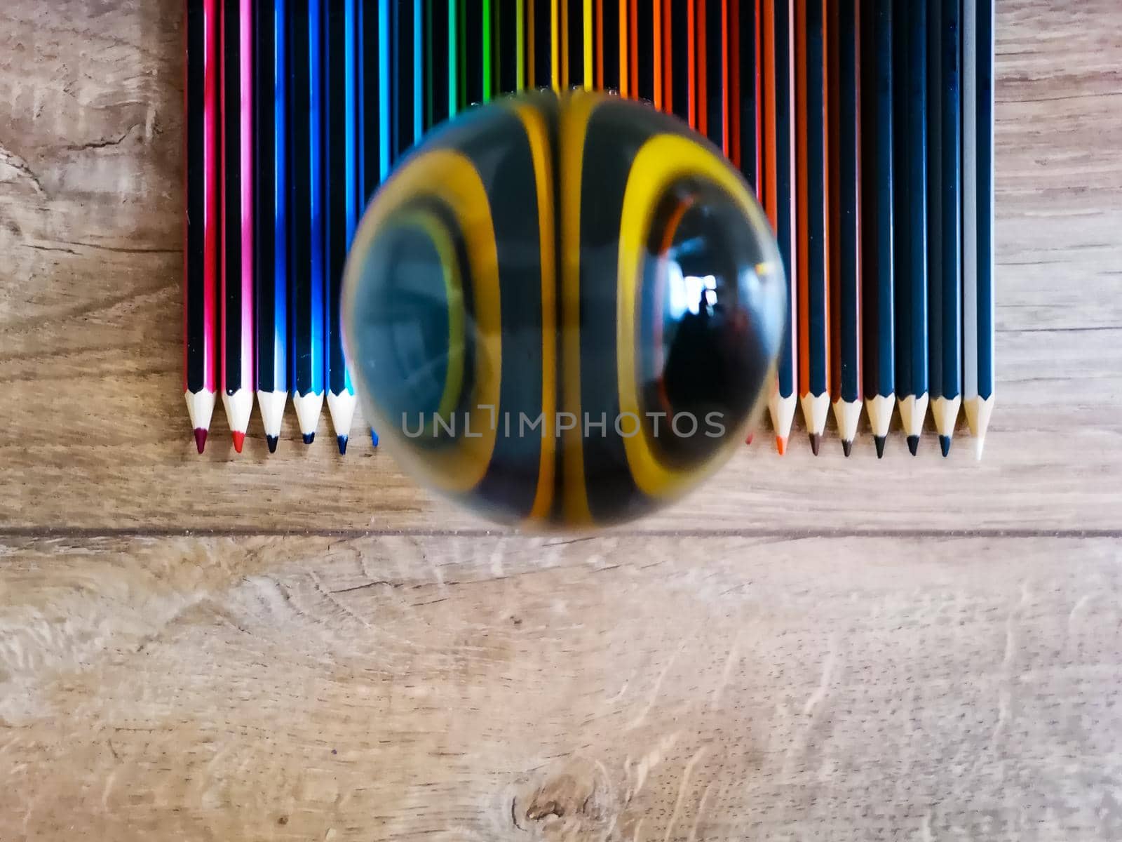 Colorful pencil crayons lie in on wooden floor with crystal glassy lensball on it