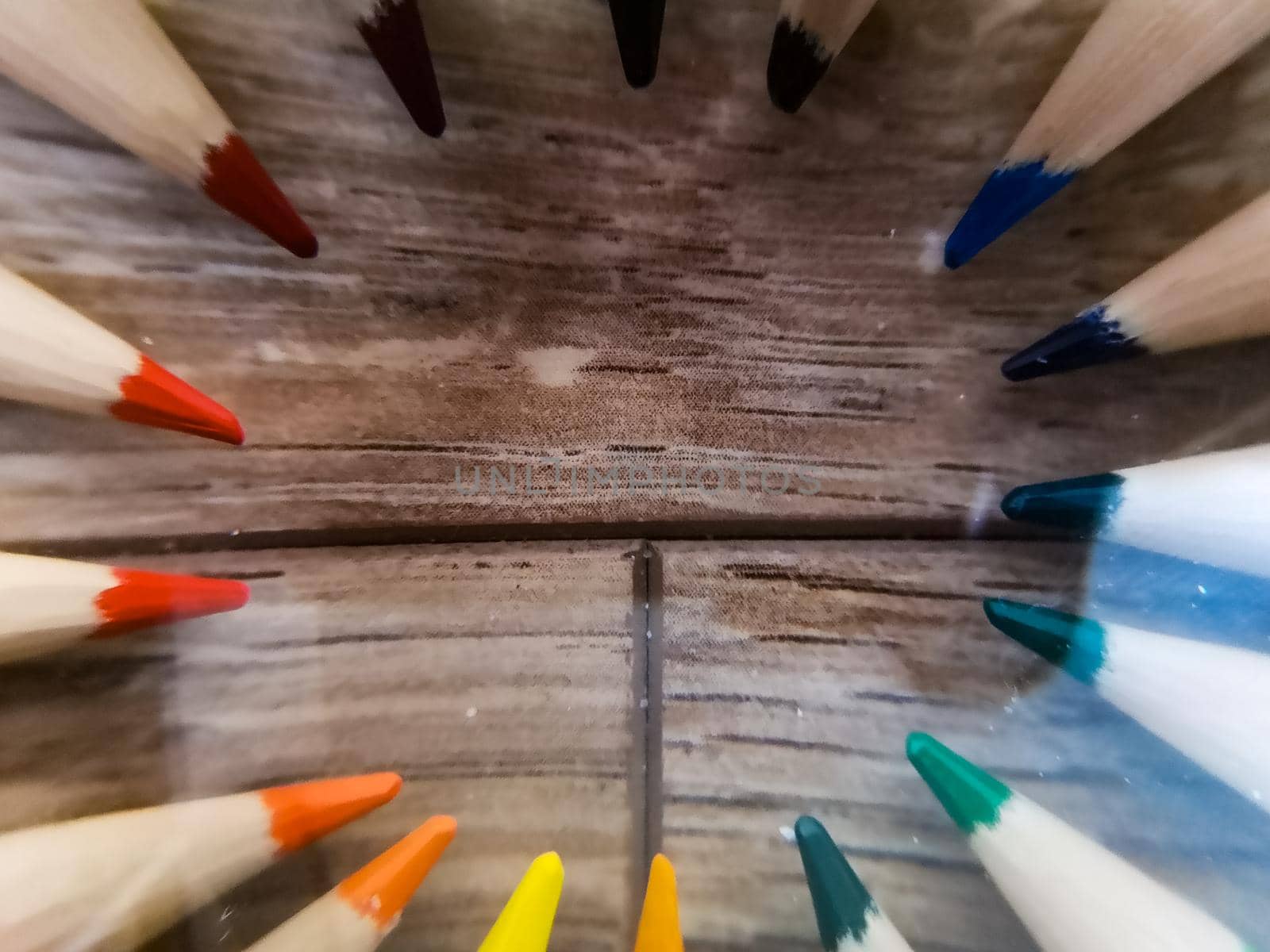 Colorful pencil crayons lie in a circle on wooden floor by Wierzchu