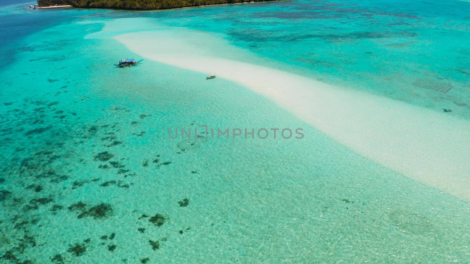 Sandy beach with tourists among turquoise waters and coral reefs. Mansalangan sandbar. Beach at the atoll. Summer and travel vacation concept. Balabac, Palawan, Philippines.