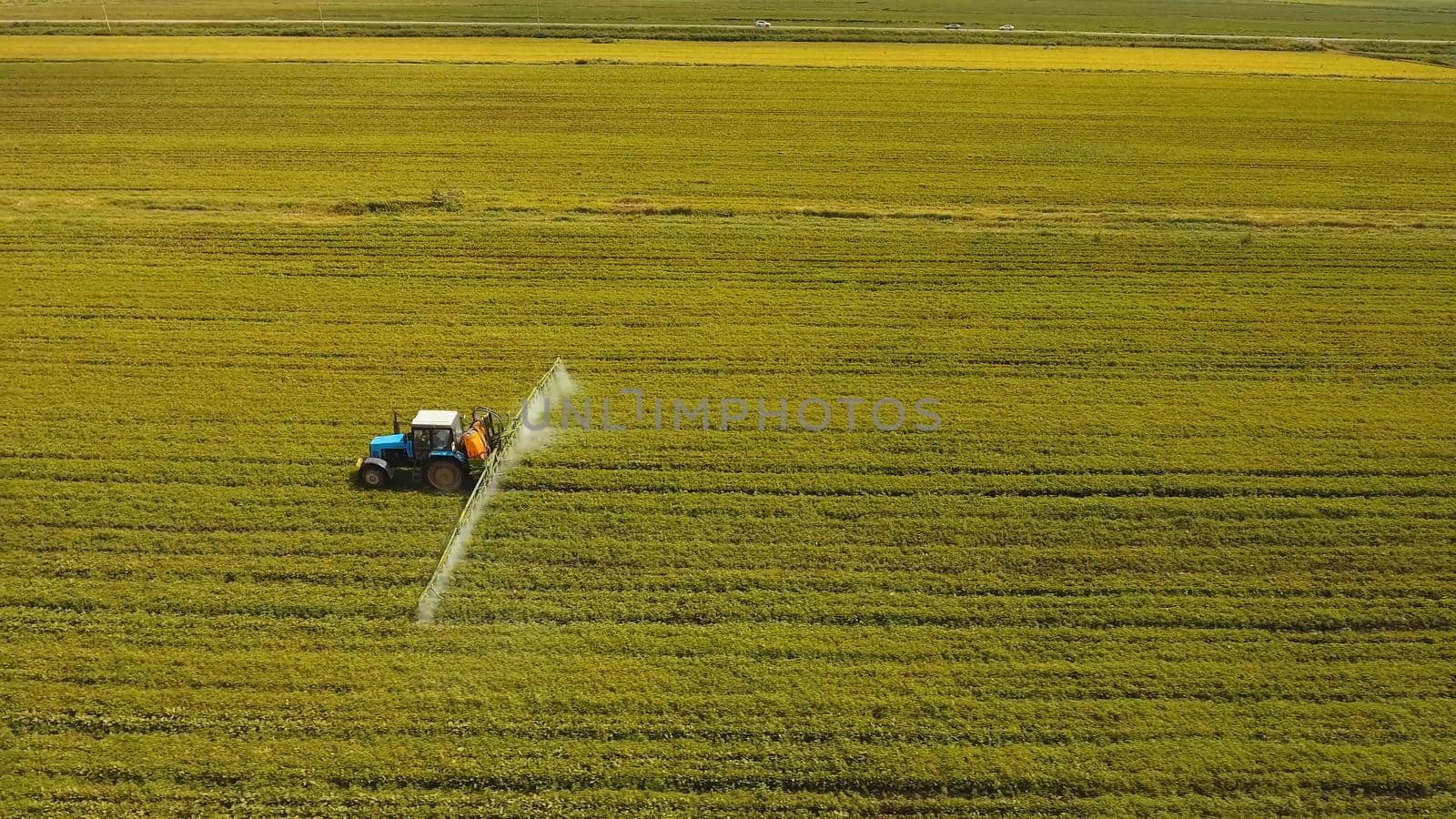 Aerial view tractor spraying the chemicals on the large green field. Spraying the herbicides on the farm land. Treatment of crops against weeds.