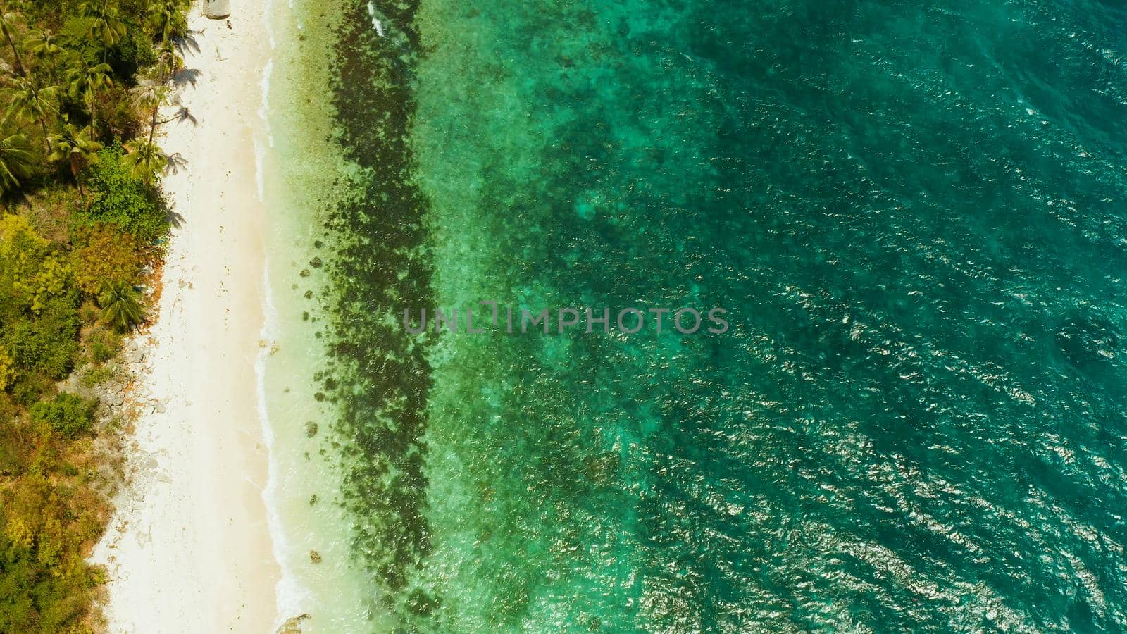 White sandy beach and azure water of the lagoon,copy space for text, top view. Ocean with waves and tropical beach. Summer and travel vacation concept