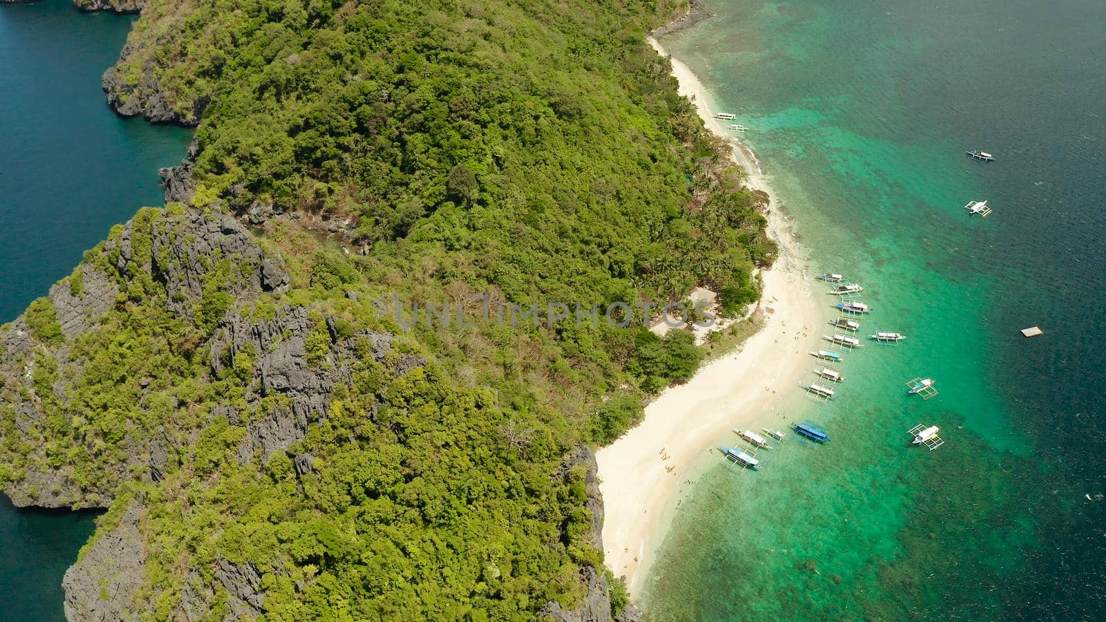 aerial view tropical beach on island with palm trees, blue lagoon and azure clear water. tourist boats on coast tropical island. Helicopter Island in El Nido, Palawan Philippines. Tropical landscape with blue lagoon, coral reef