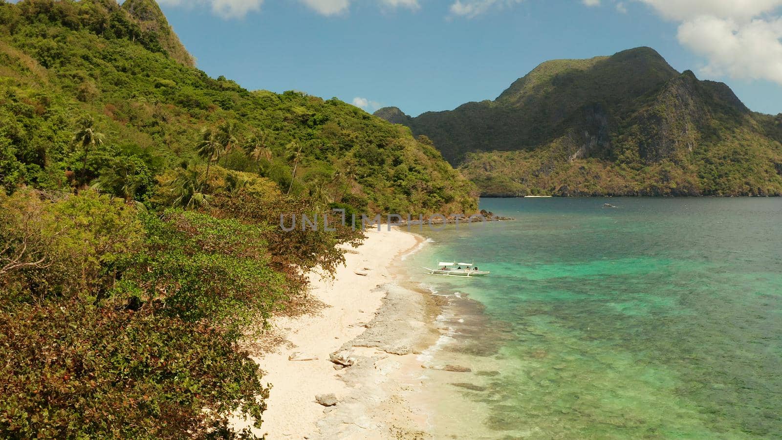 aerial view tropical beach on island with palm trees, blue lagoon and azure clear water. Helicopter Island in El Nido, Palawan Philippines. Tropical landscape with blue lagoon, coral reef