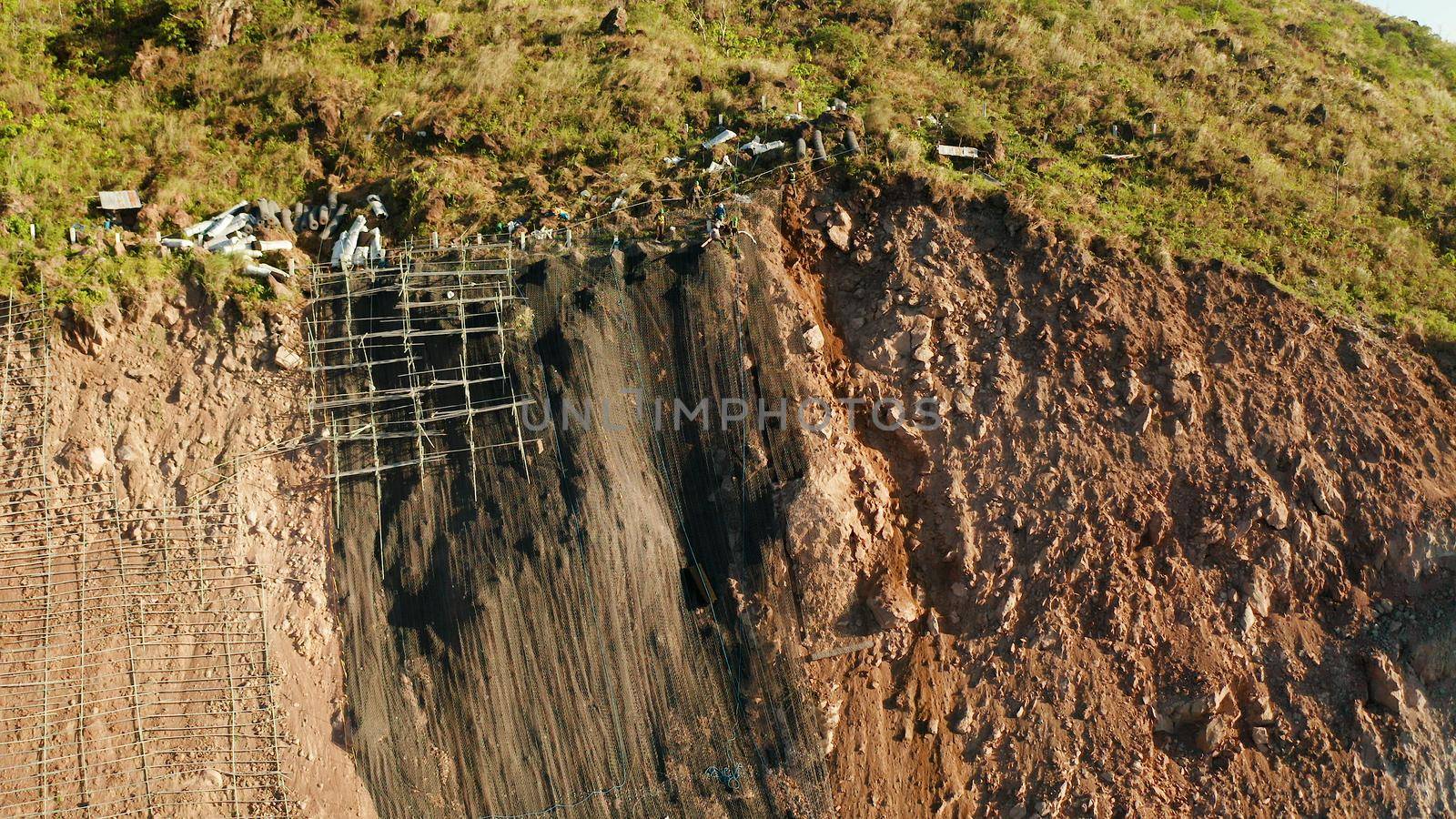 Protection of road from mountain slough, rockfall with metal accumulative restraining net fences. Workers constructing anti-landslide concrete wall prevent protect against rock slides. Rockfall protection. Workers strengthen the slope of the mountain with steel grid preventing rockfall and landslide on the road.