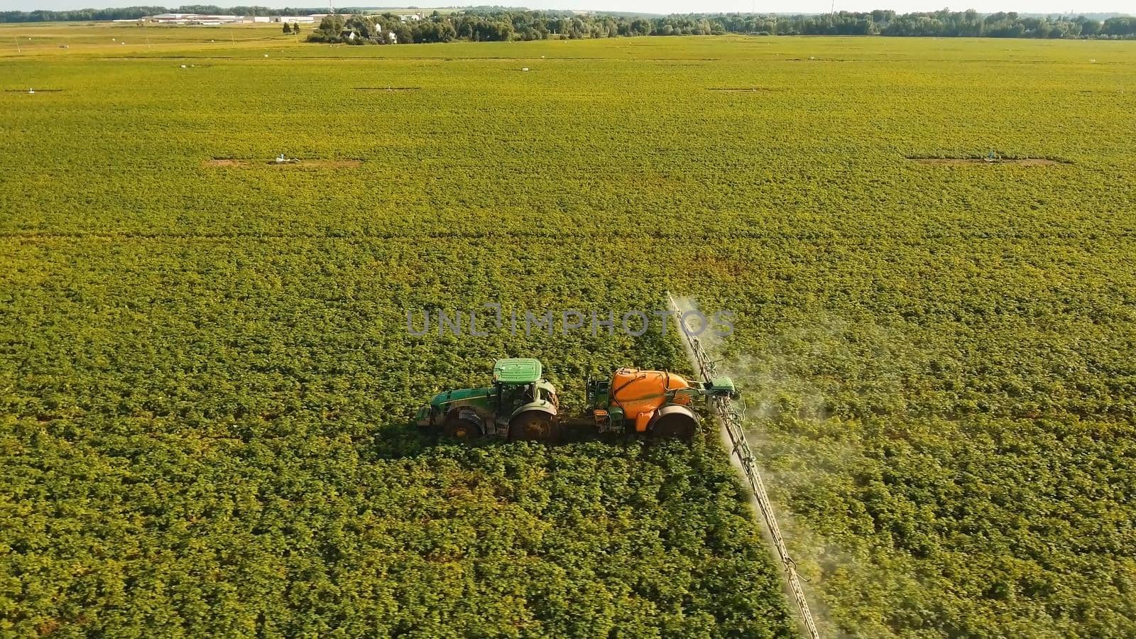 Aerial view tractor spraying the chemicals on the large green field. Spraying the herbicides on the farm land. Treatment of crops against weeds.