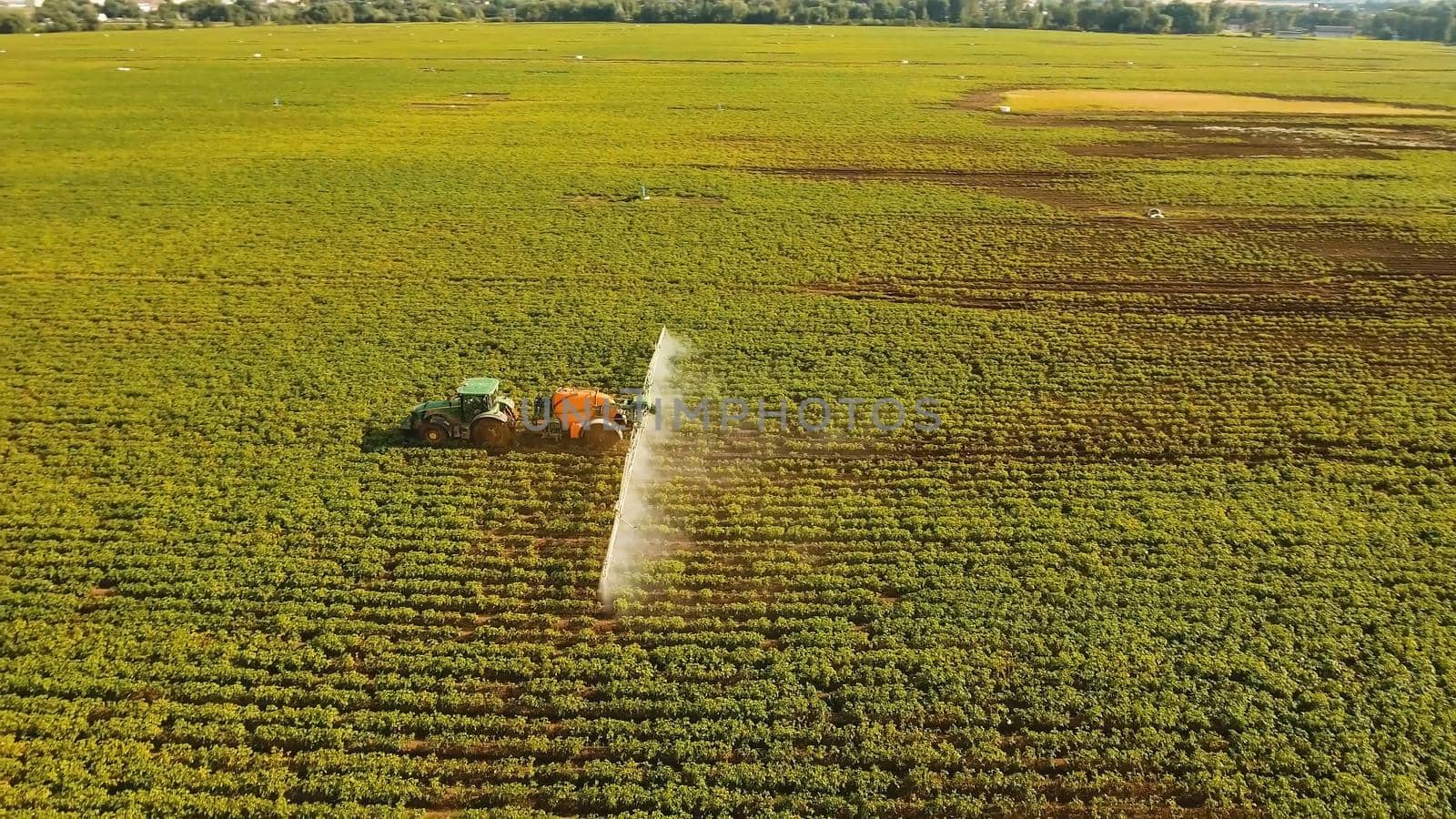 Aerial view tractor spraying chemicals on large green field. Spraying the herbicides on the farm land. Treatment of crops against weeds.