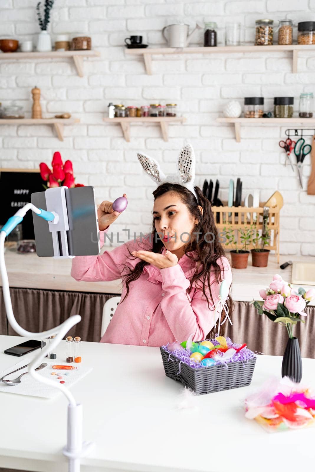 Funny woman greeting her friends online, celebrating easter, covering her eyes with colorful eggs