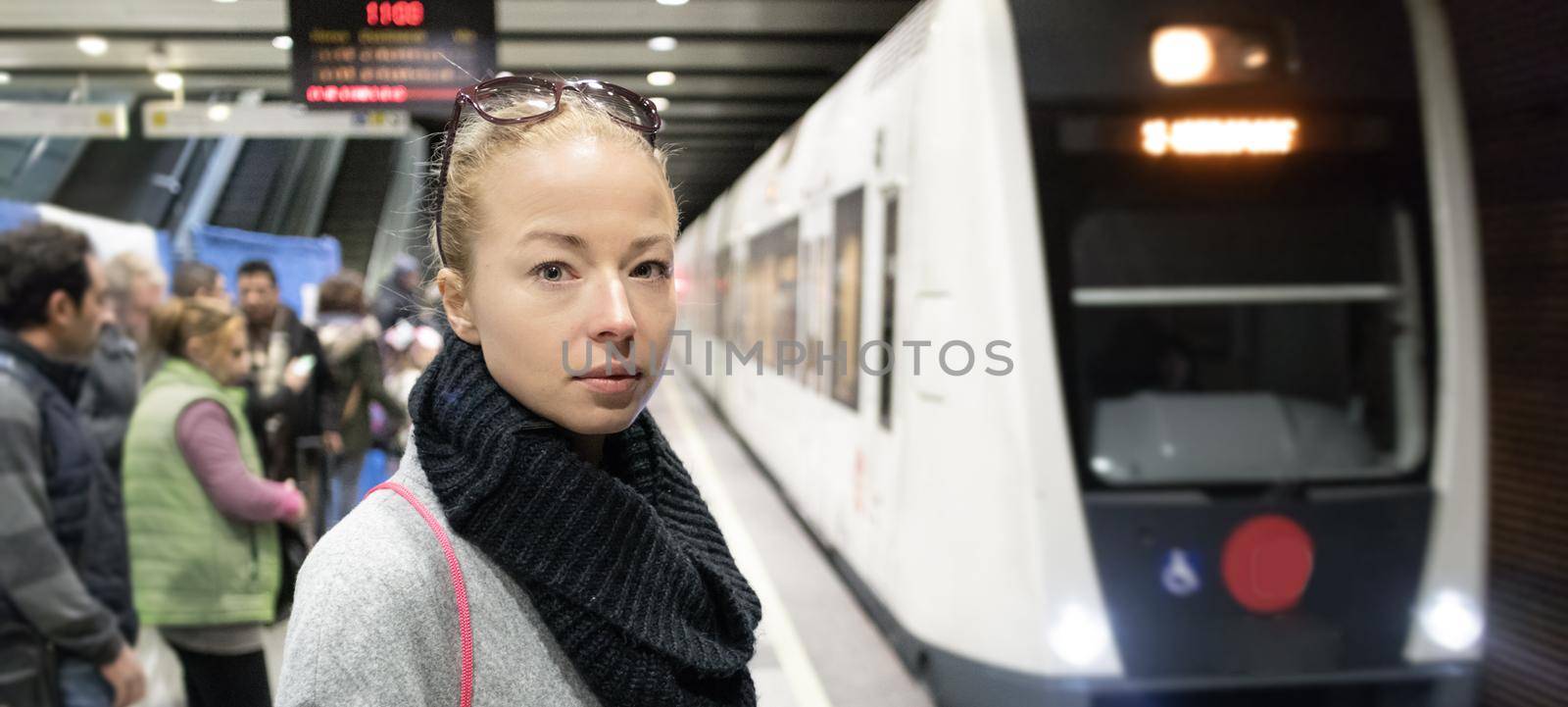 Young woman in winter coat waiting on the platform of a railway station for train to arrive. Public transport by kasto