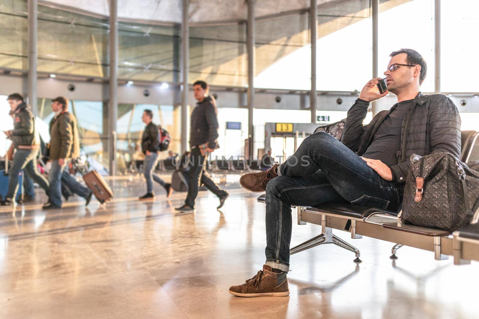 Casual young man talking on cell phone while waiting to board a plane at airport departure gates.