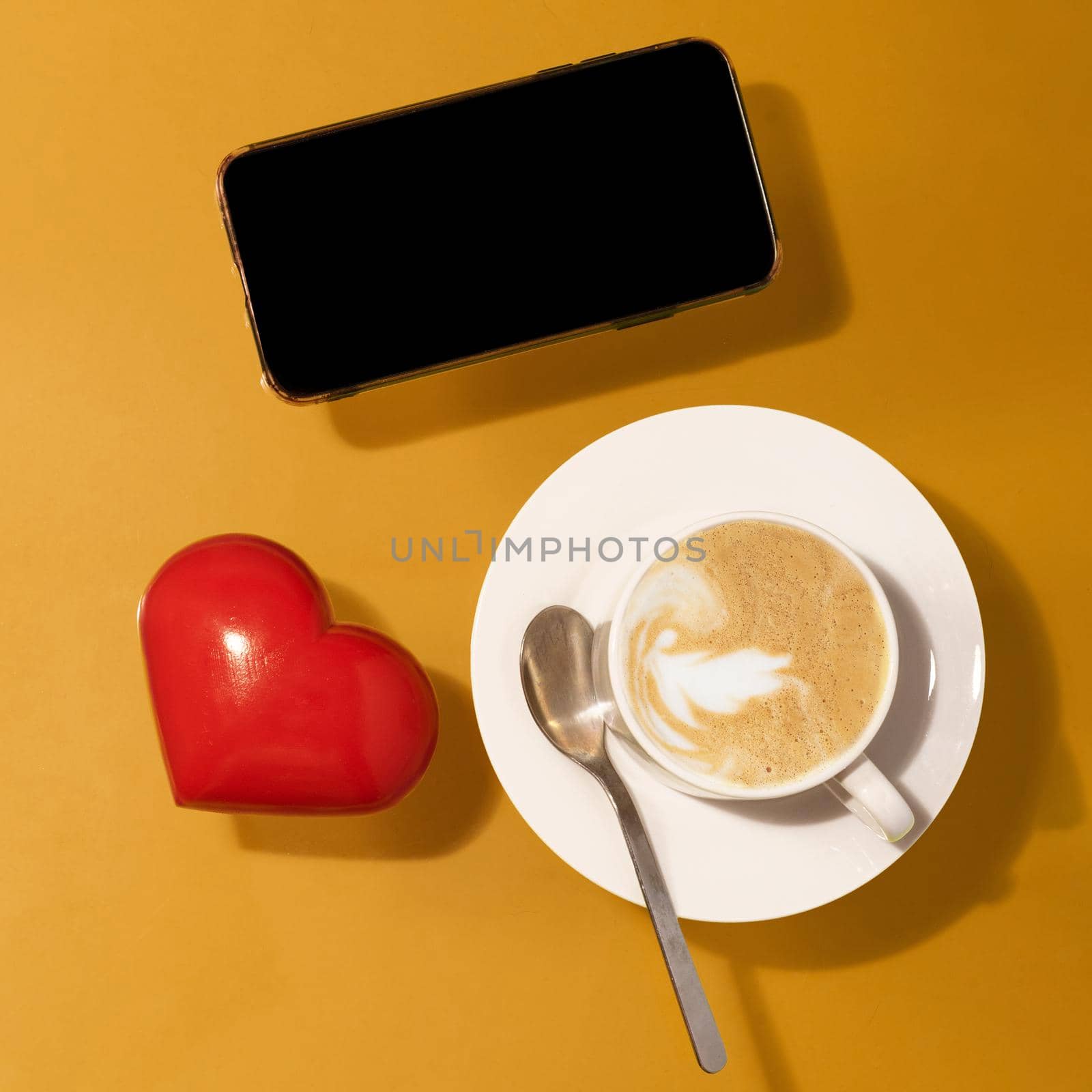 cup of coffee with chocolate, red heart, phone on a table
