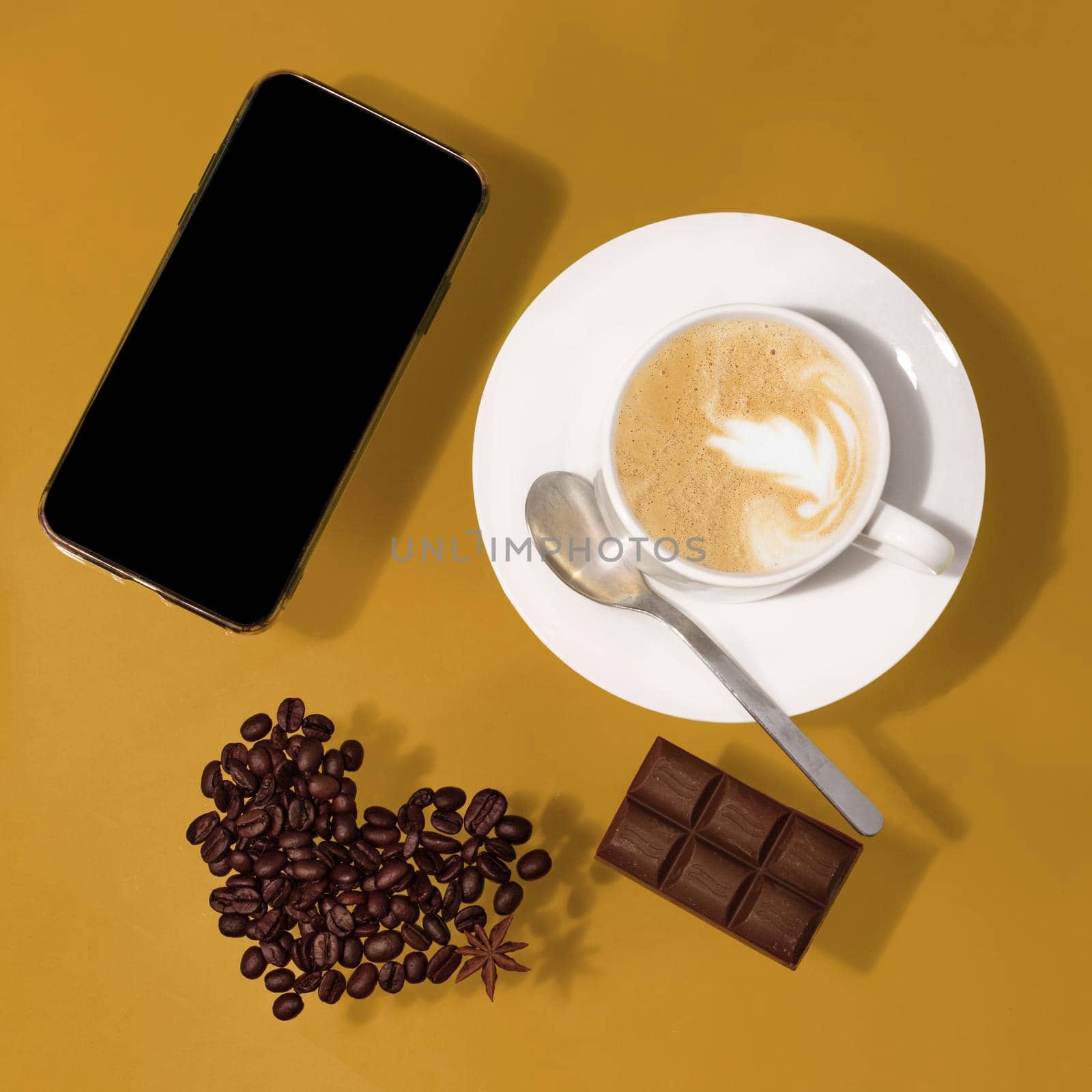 cup of coffee with chocolate, heart shape beans, phone on a table by Iryna_Melnyk