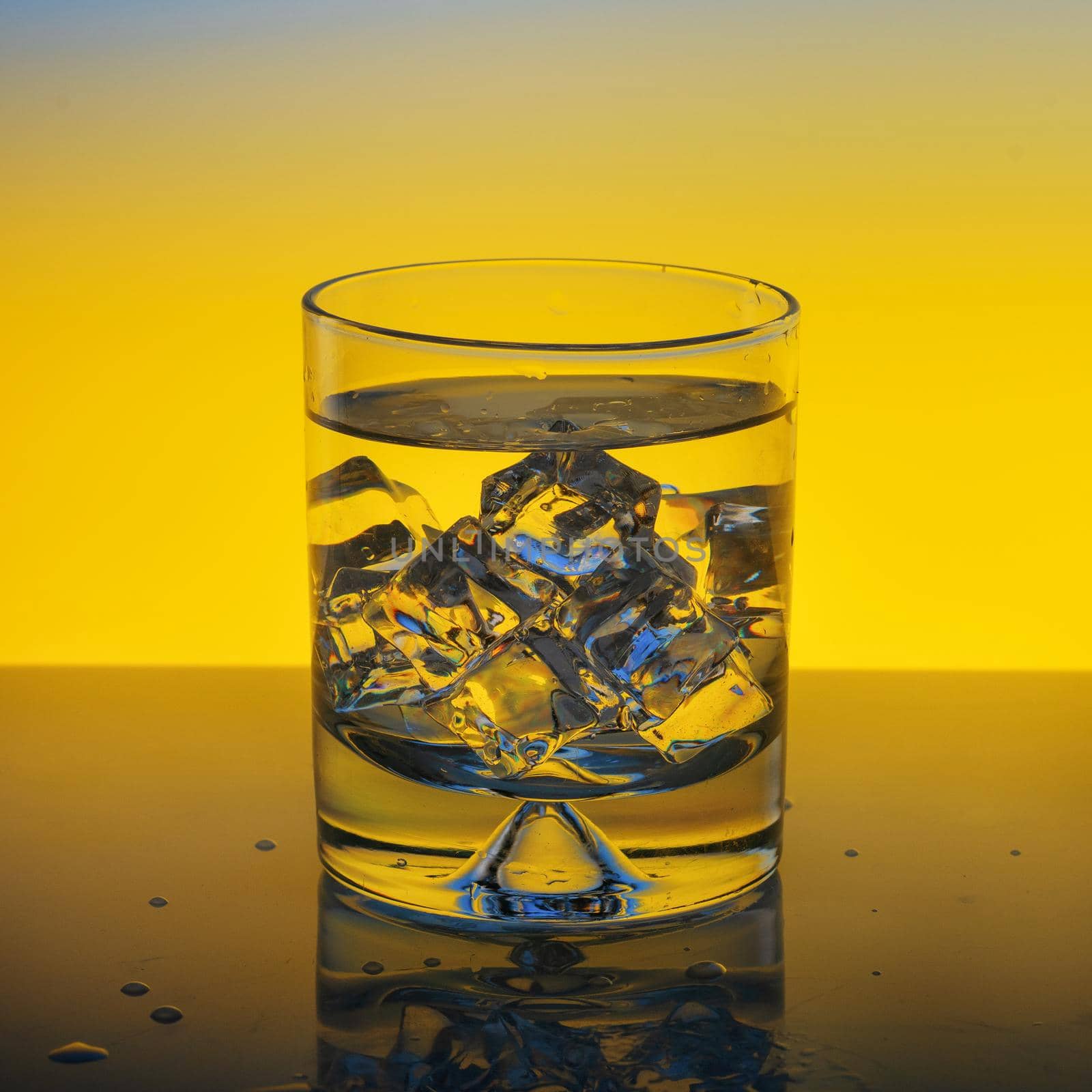 glass with water and ice on yellow background