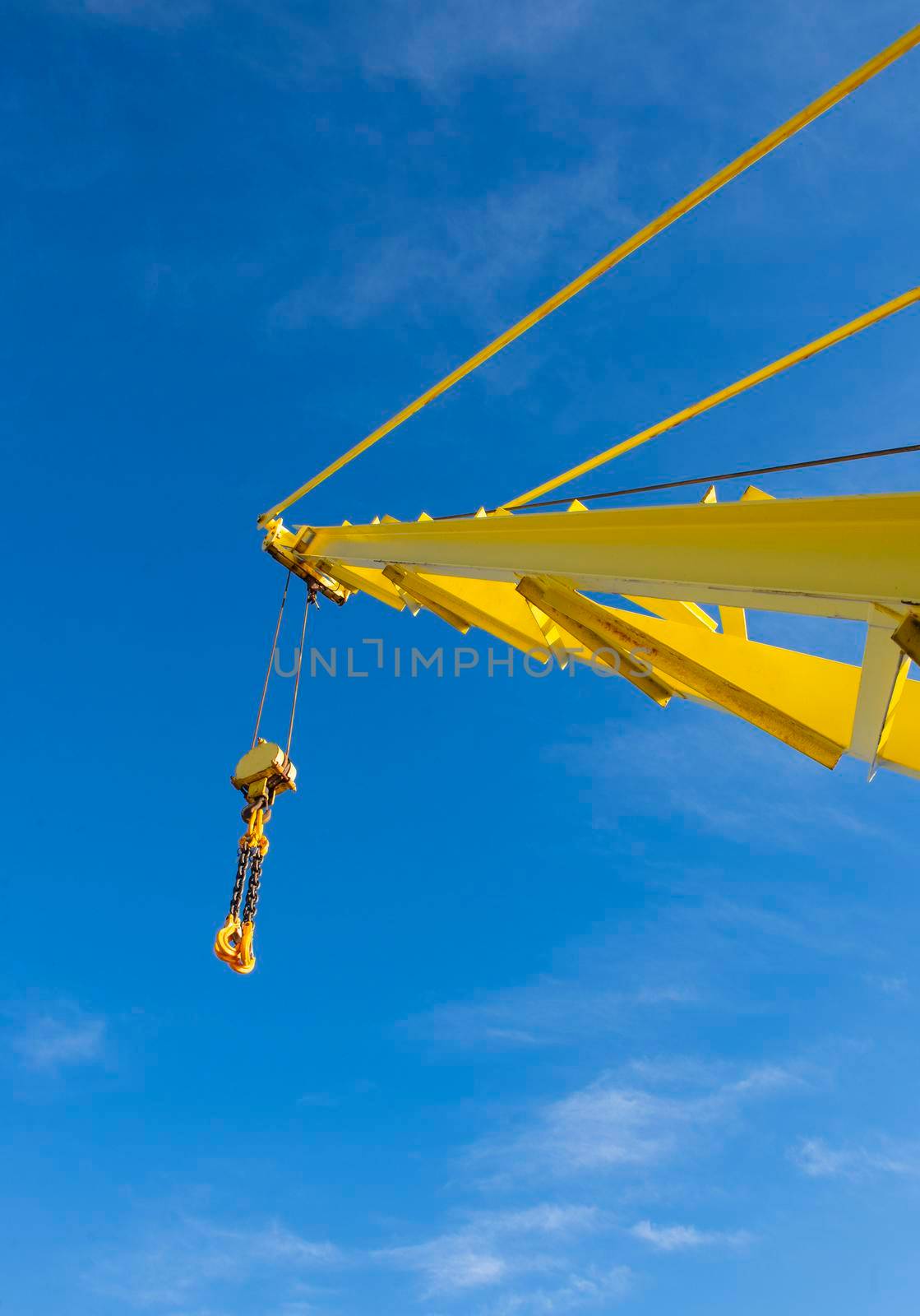Large extended industrial crane jib boom arm against a blue sky background with block tackle