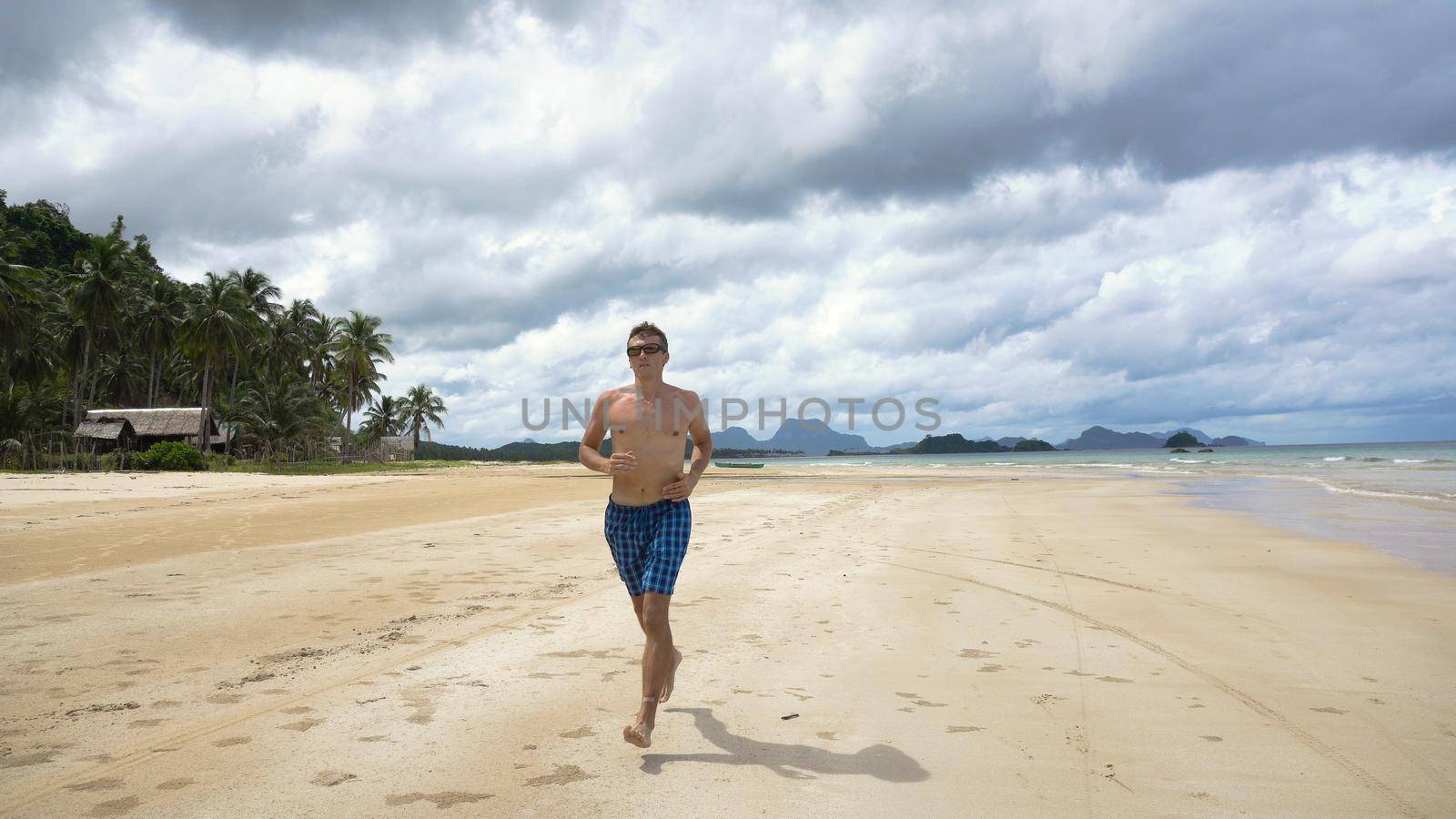 Man running along beach. Fitness sports runner man jogging on beach. Handsome young fit sporty male athlete running outside on beautiful beach training.