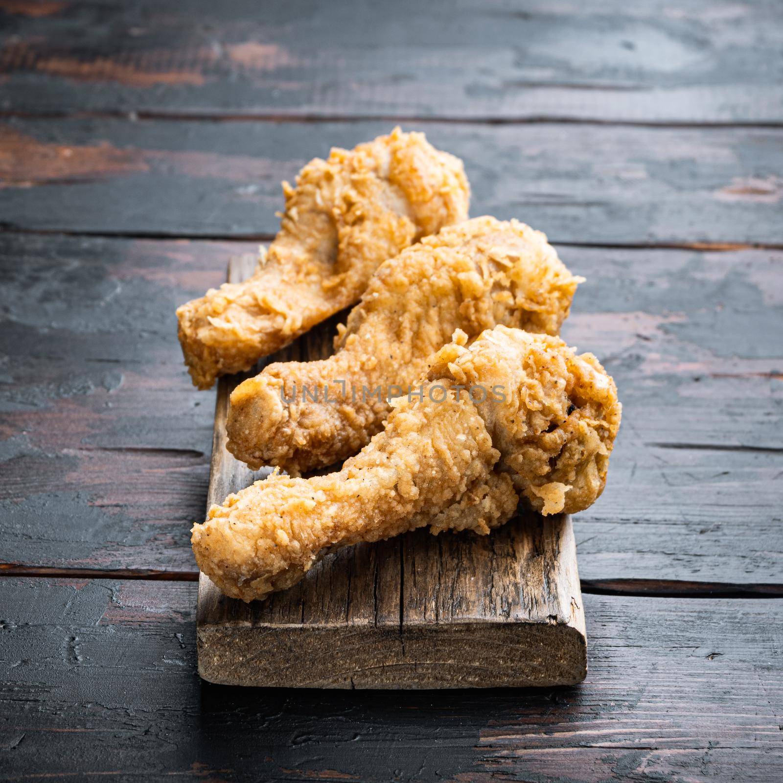 Fried crispy chicken legs, drumstick parts on dark wooden background.