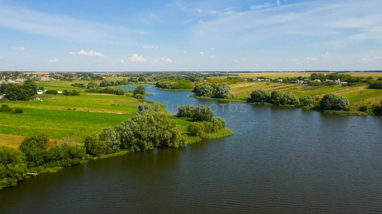 The river flows through the countryside surrounded by green meadows in the summer.
