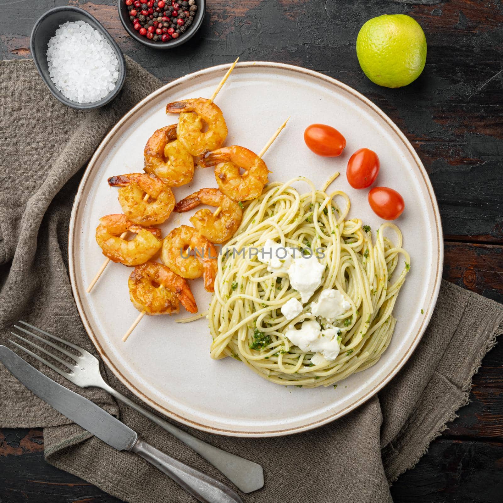 Spaghetti with green pesto and shrimps skewers set, on plate, on old dark wooden table background, top view flat lay