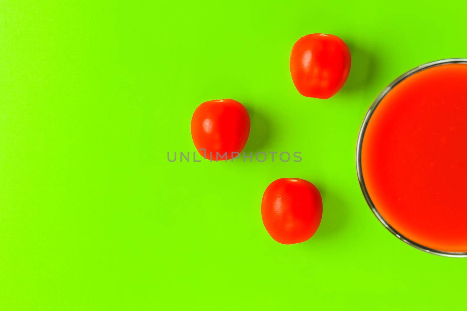 red tomato and a glass of tomato juice on a green background. hard shadow. isolate by roman112007
