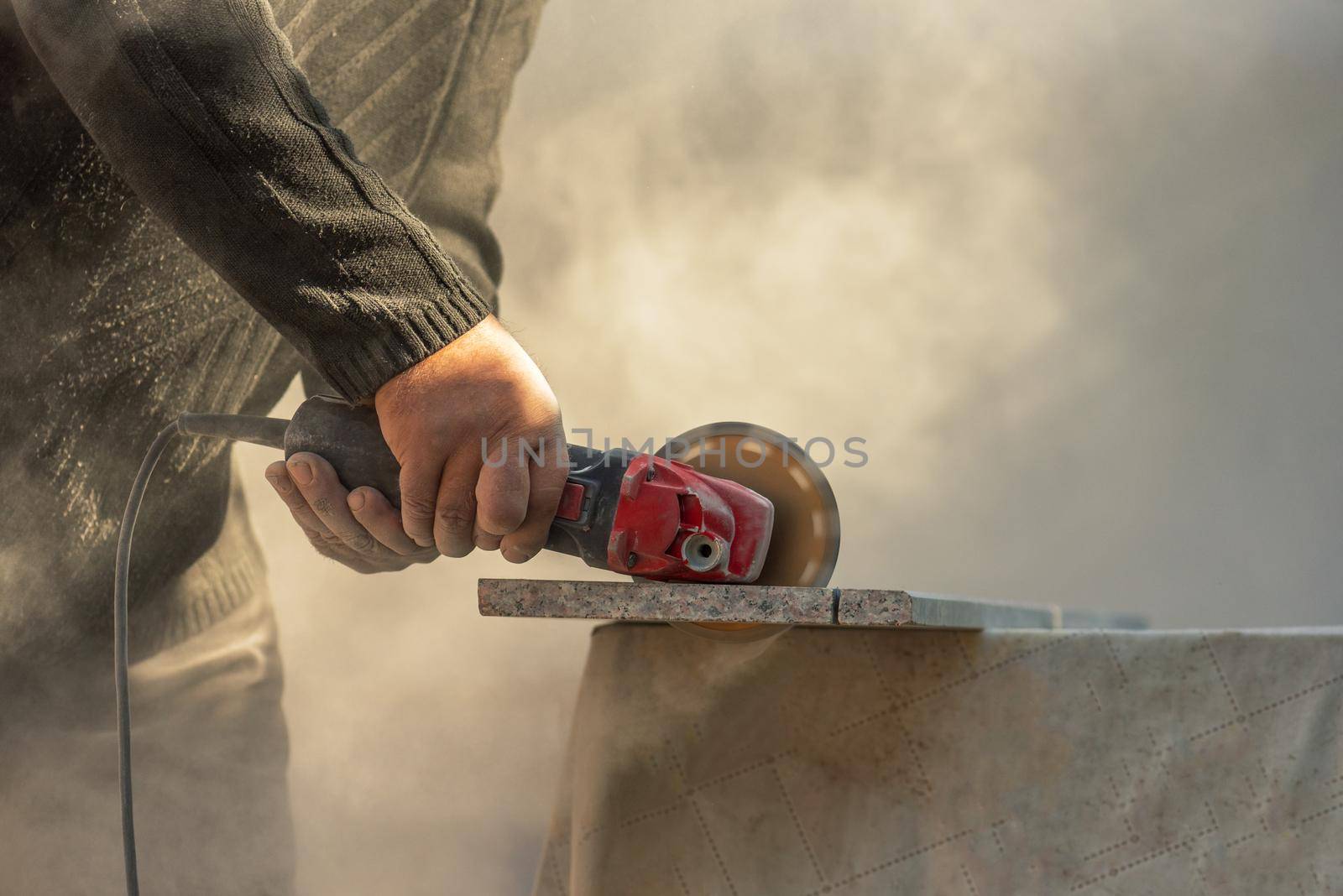 Grinder worker cuts stone block with electric hand saw.