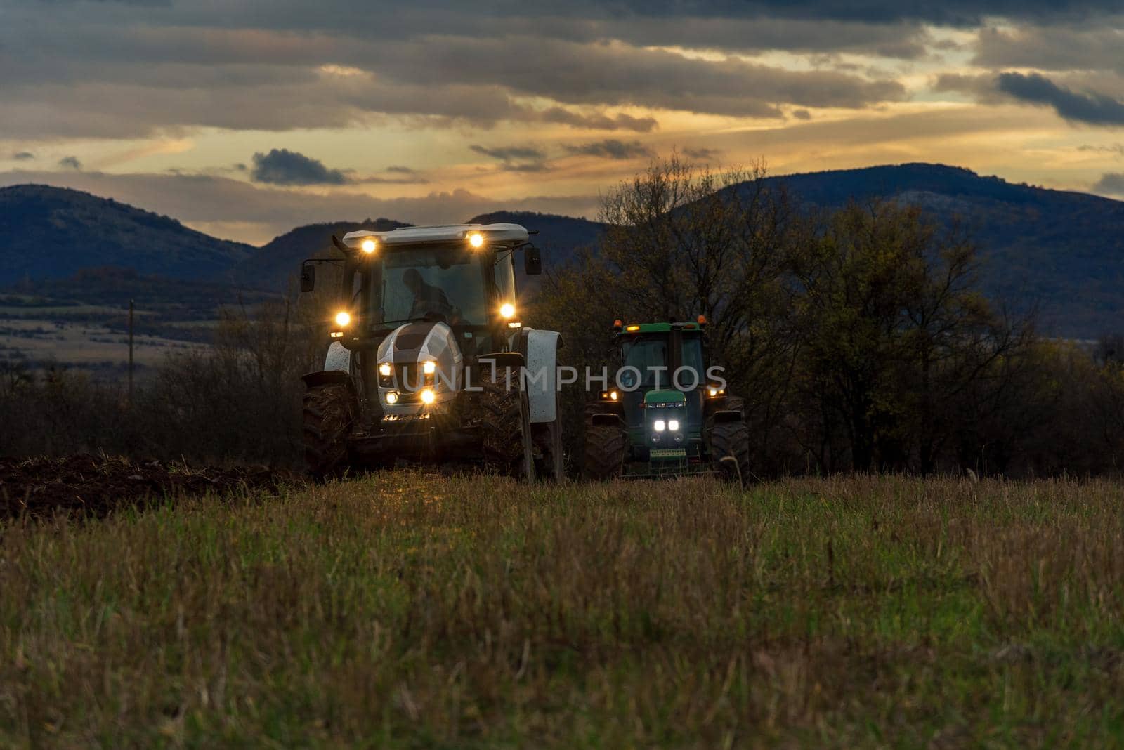 Farmer in tractor preparing land with cultivator at night