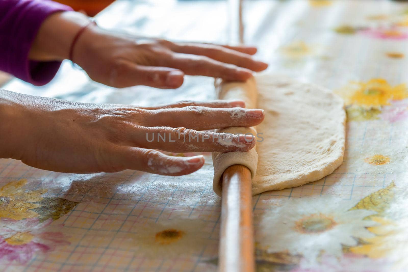 female hands rolling raw dough on white table at home