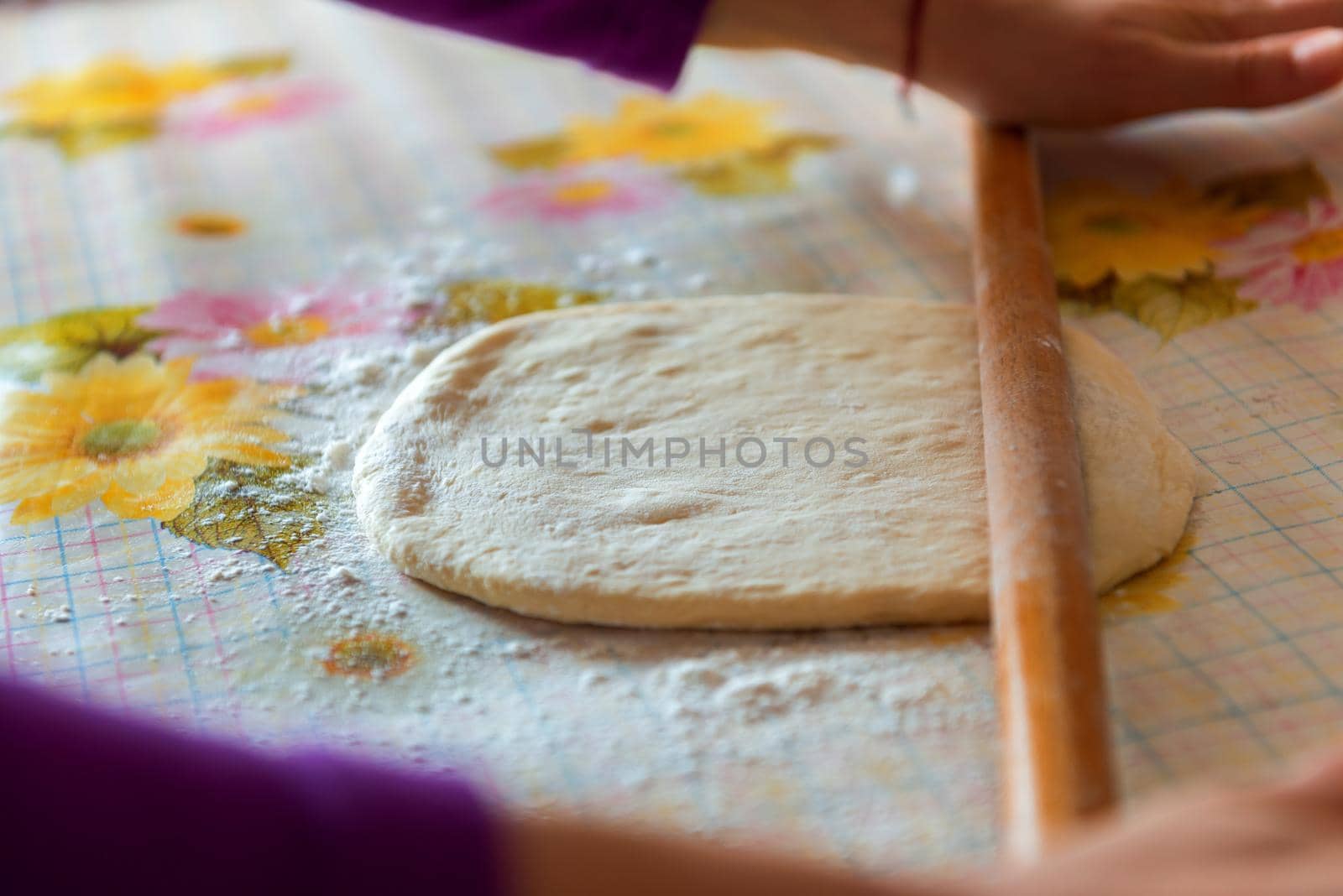 female hands rolling raw dough on white table at home