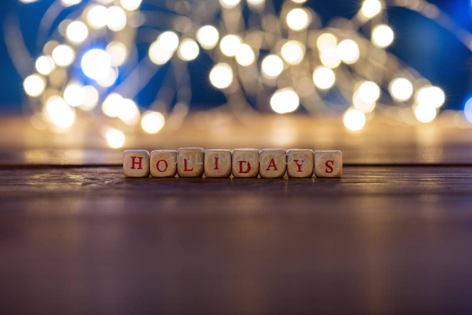 Happy holidays written on a rustic wooden panel. With background lights.