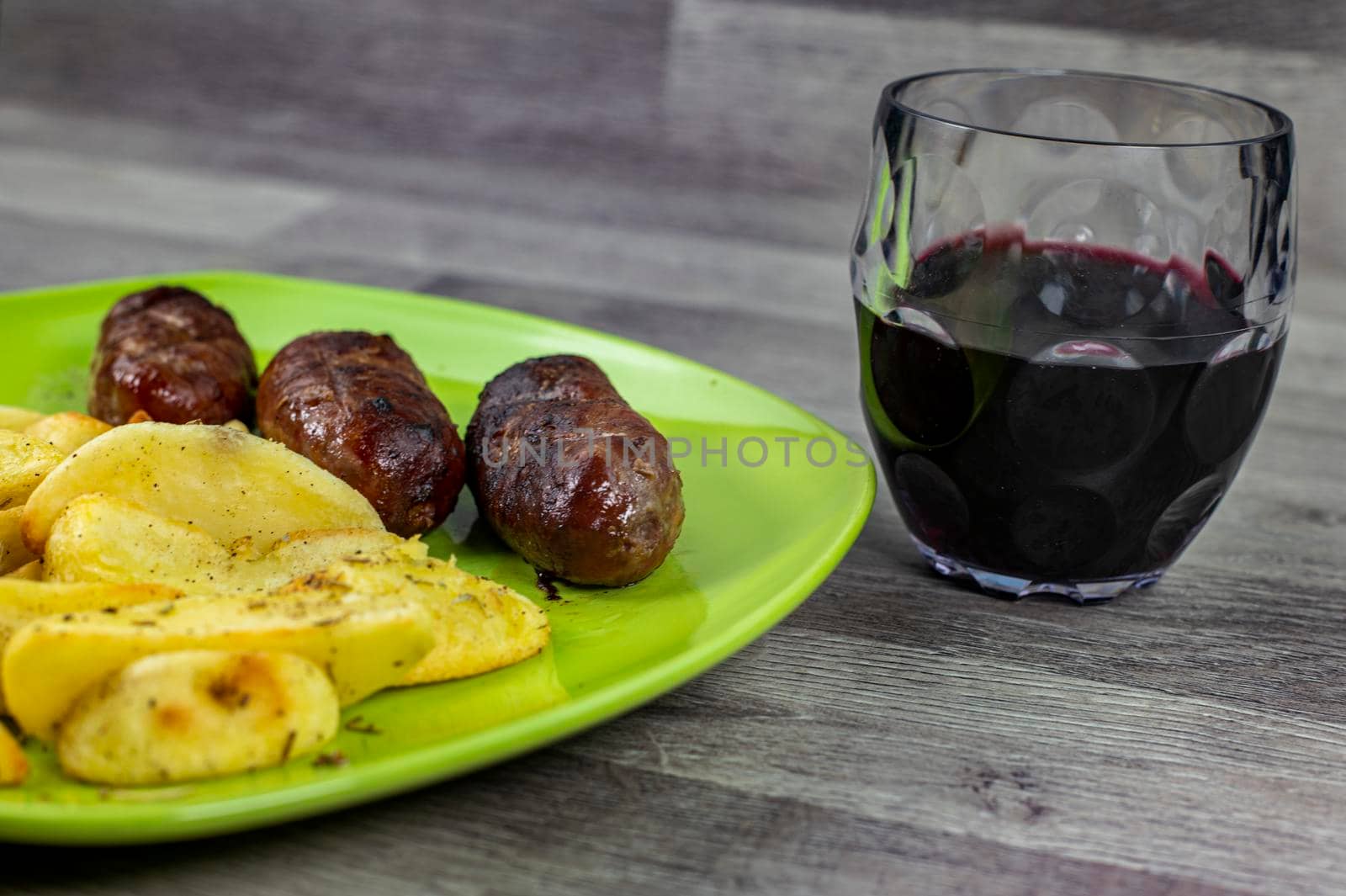 plate sausages potatoes and glass of wine on wooden background