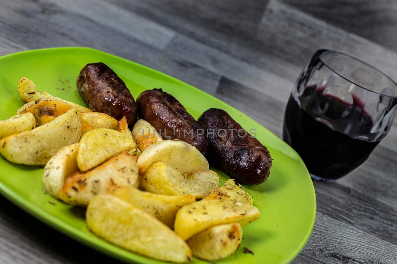 plate sausages potatoes and glass of wine on wooden background
