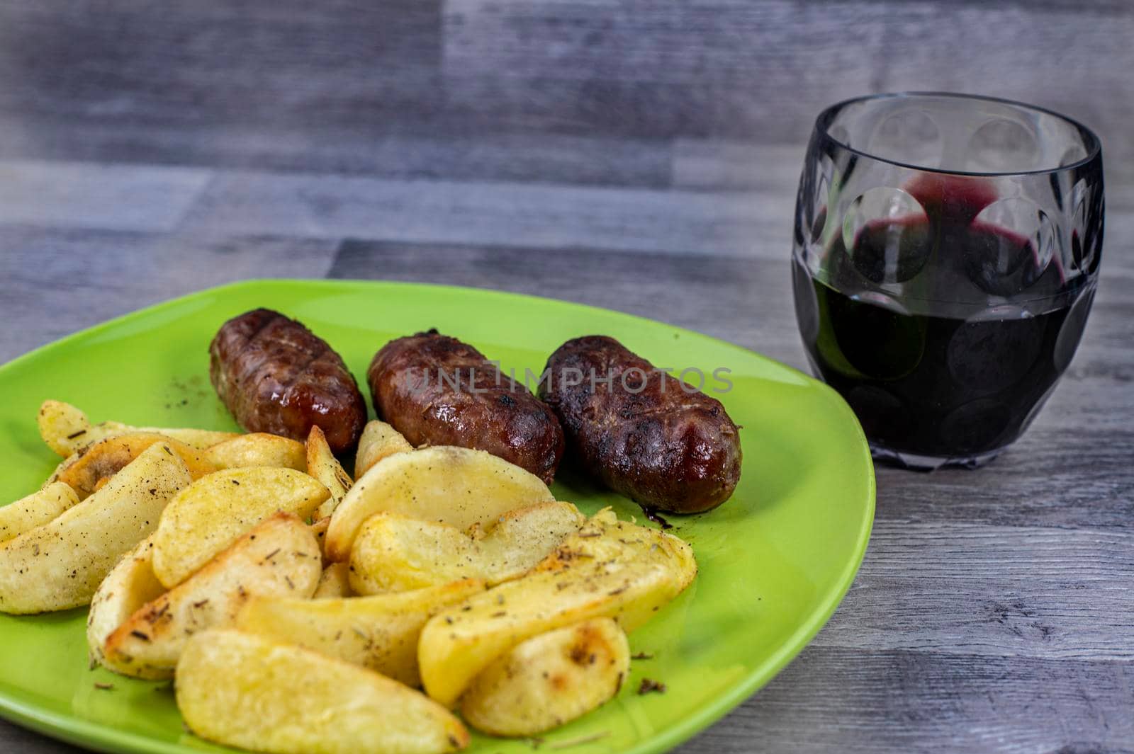 plate sausages potatoes and glass of wine on wooden background