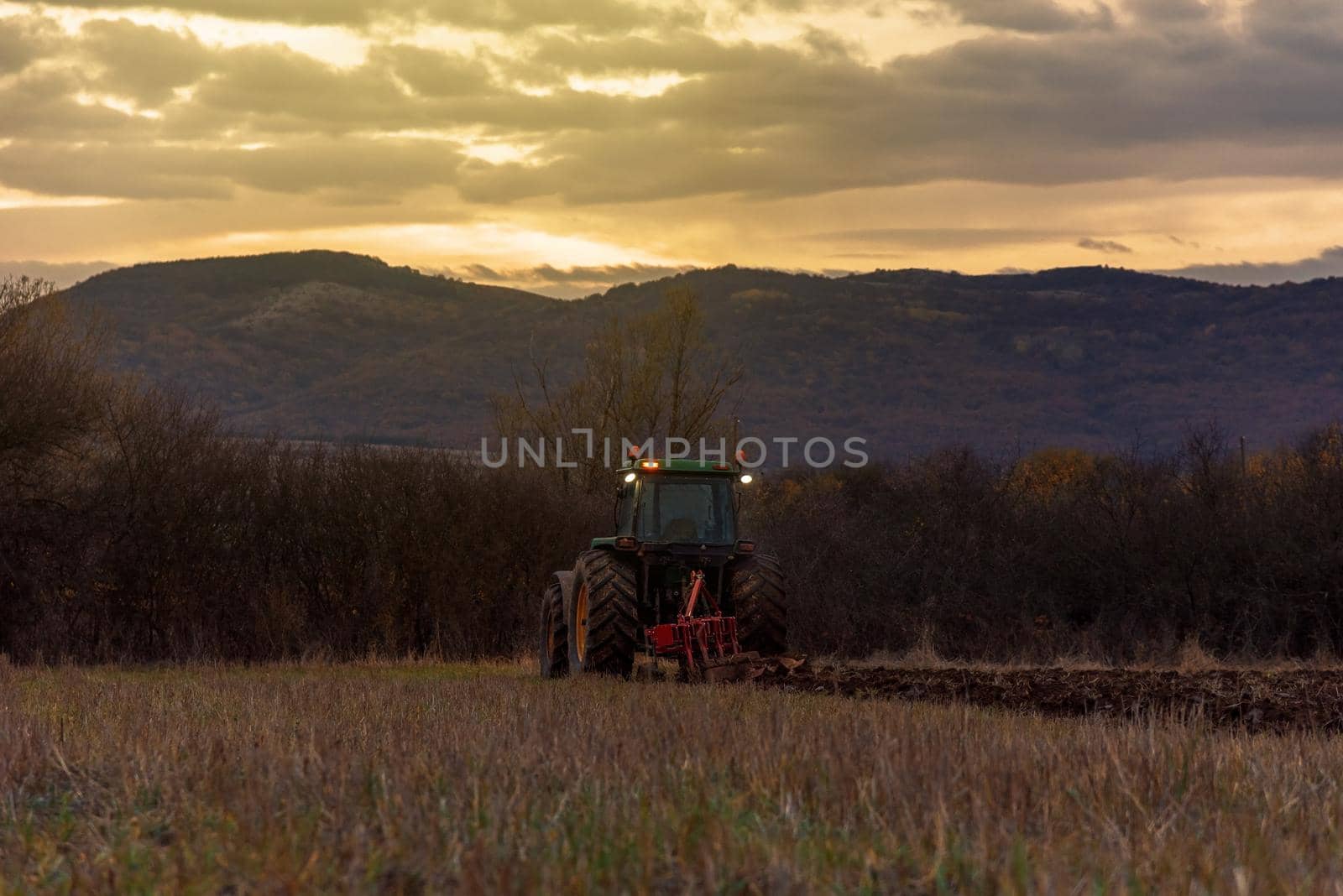 Tractor plowing fields at sunset.