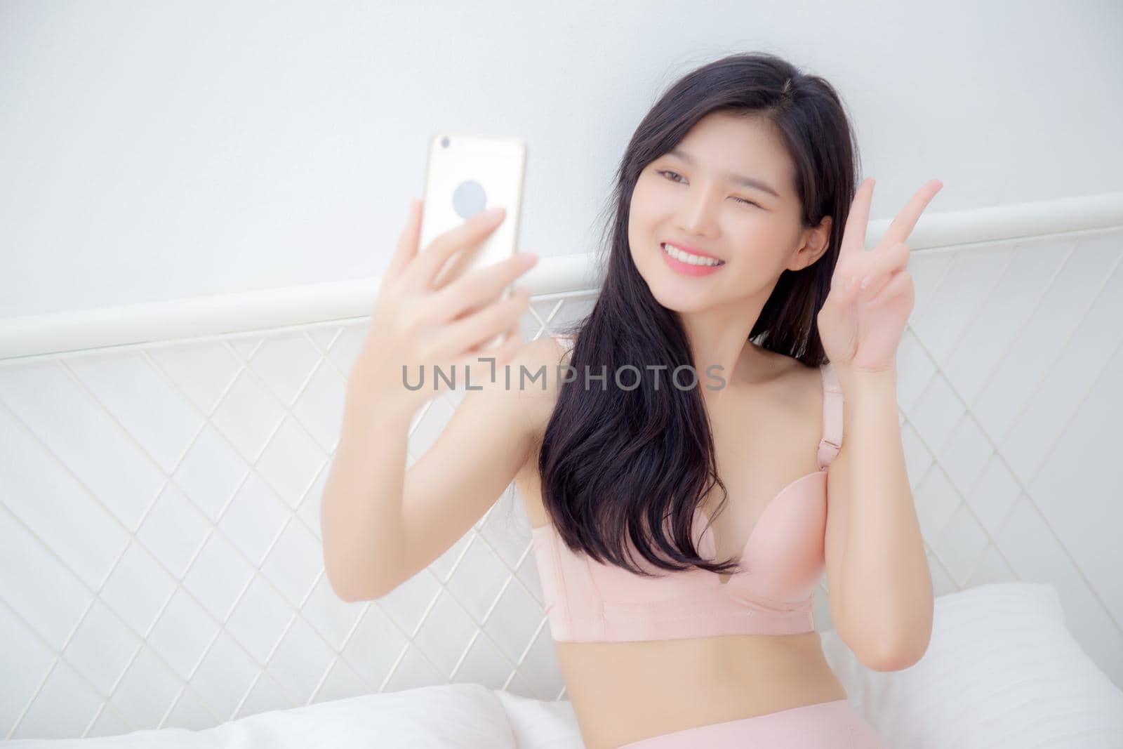 Beautiful young asian woman sexy in underwear talking a selfie on smartphone for social network in the bedroom, girl in lingerie relax with taking a picture on mobile phone on bed in the bedchamber.