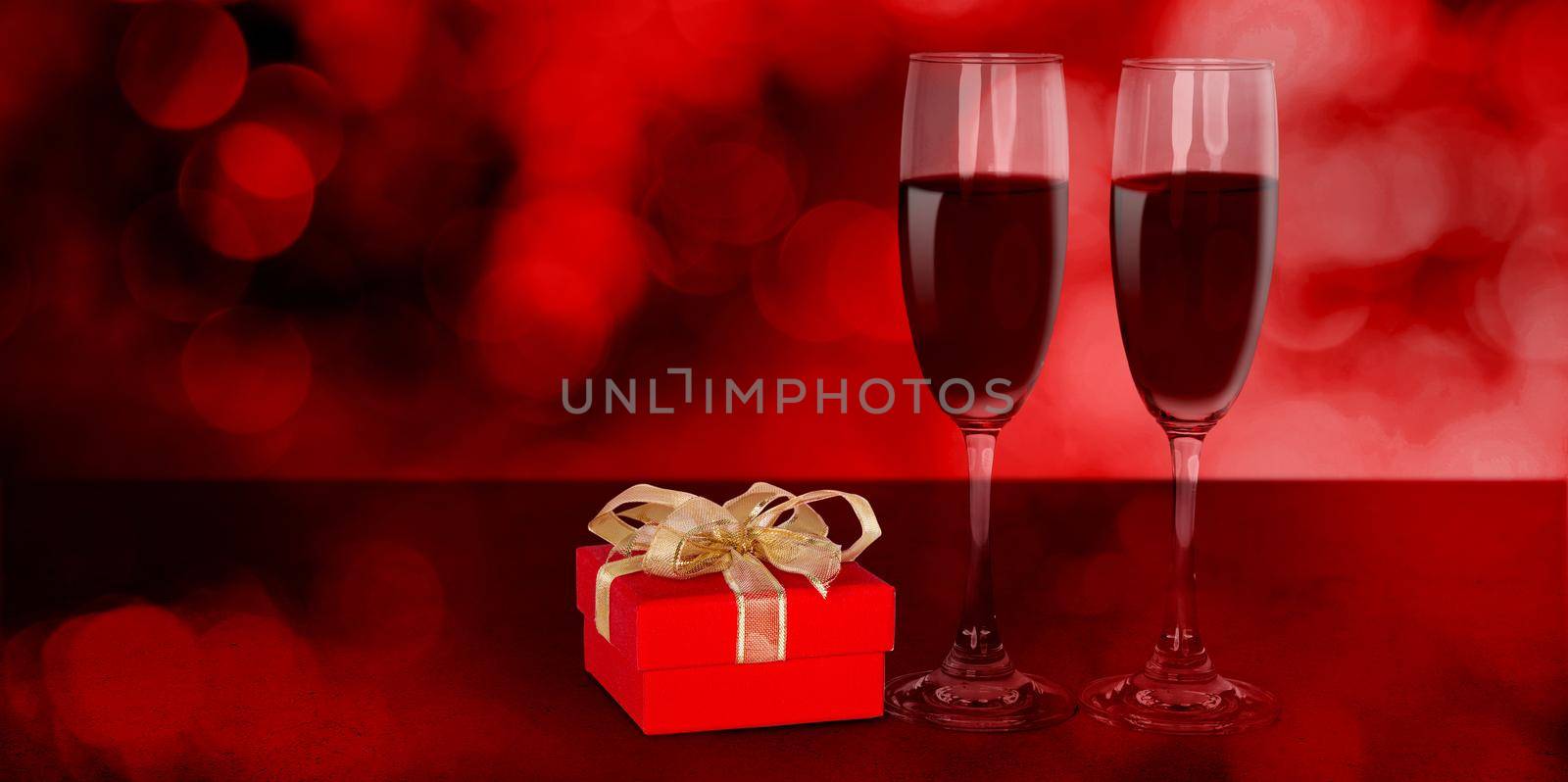 Two wineglasses and red gift box on desk with red blur bokeh background, champagne glasses and presents with celebration and anniversary, love and romantic, valentine day concept. by nnudoo