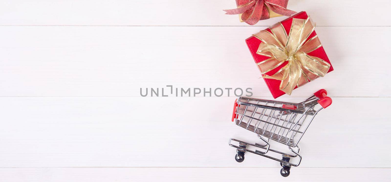 Cart of supermarket and gift box on wooden table, shopping online for presents in valentine day, trolley for sale commerce in holiday and vacation, copy space, celebration and anniversary concept. by nnudoo