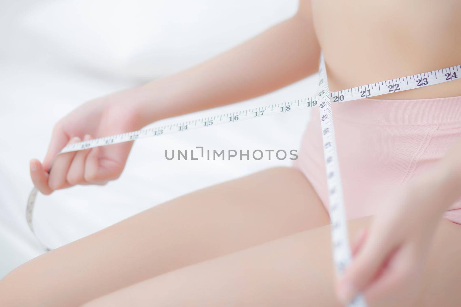 Beautiful young asian woman sexy body slim measuring abdomen for control weight loss in the room, beauty girl belly thin have cellulite with tape measure for diet, health and wellness concept.