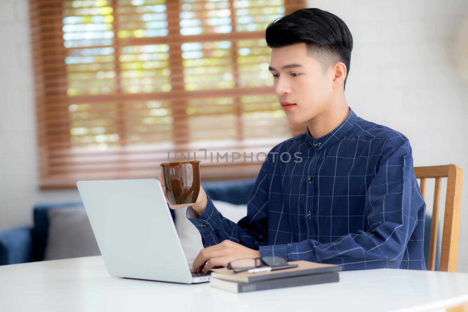 Young business man working from home with laptop computer on desk, freelance male sitting stay home using notebook for communication and relax on table, entrepreneur in startup business, new normal.