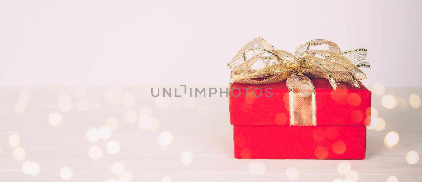 Red gift box on wooden table with bokeh background, love and romance, presents in celebration and anniversary with surprise on desk, happy birthday, copy space, nobody, valentine day concept.