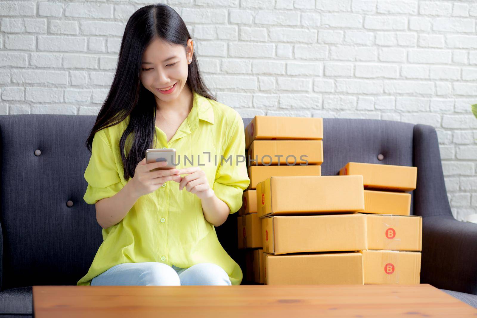 Young asian woman is entrepreneur check order from smartphone with customer while purchase online, logistic and delivery, online shopping, female is seller of business SME, merchant looking phone.