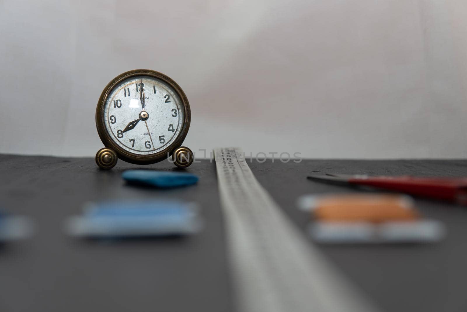 Clock surrounded by sewing utensils such as needle, thread and sewing tape measure.