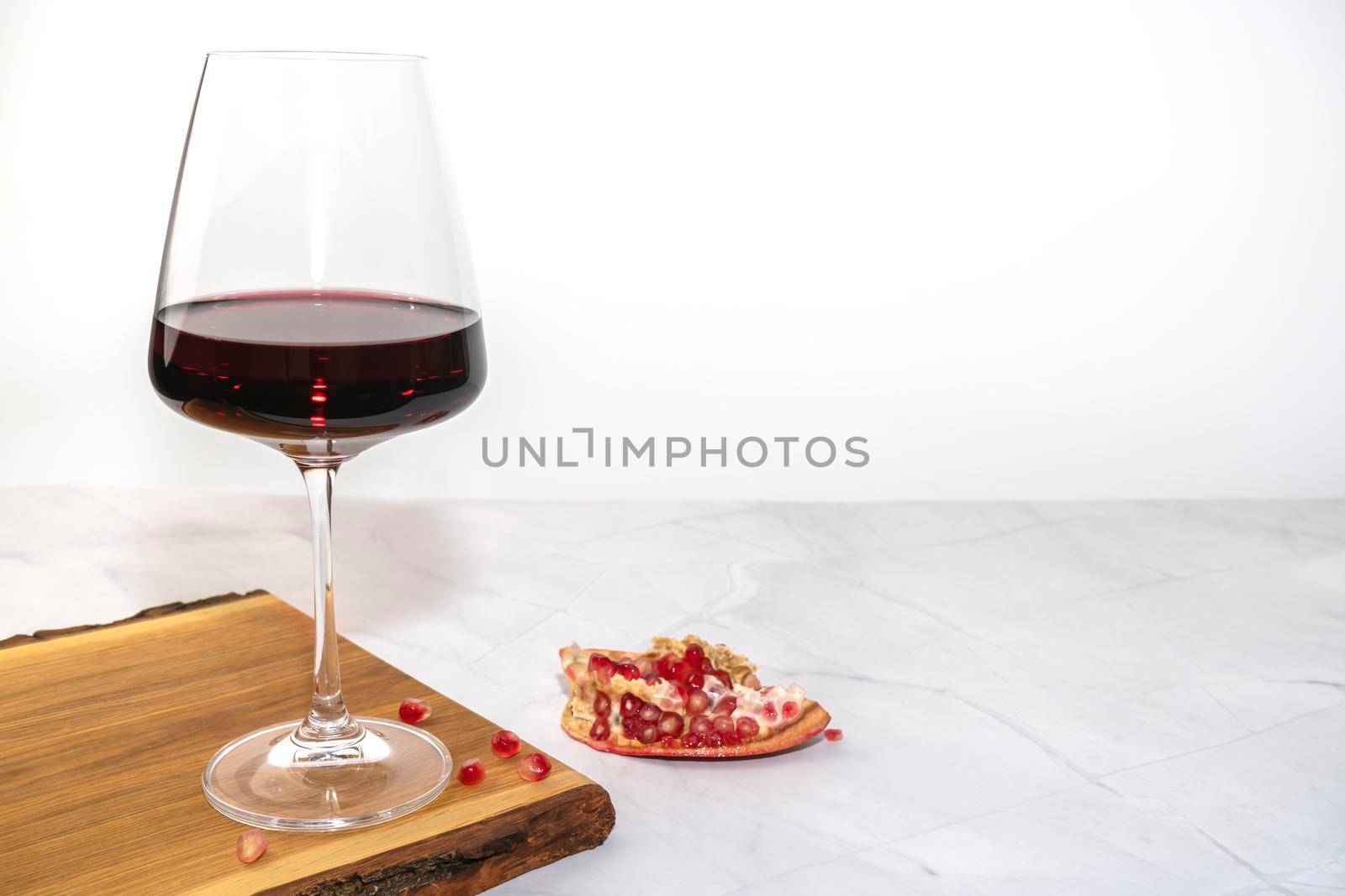 a glass of red wine on a Board with pomegranate by roman112007