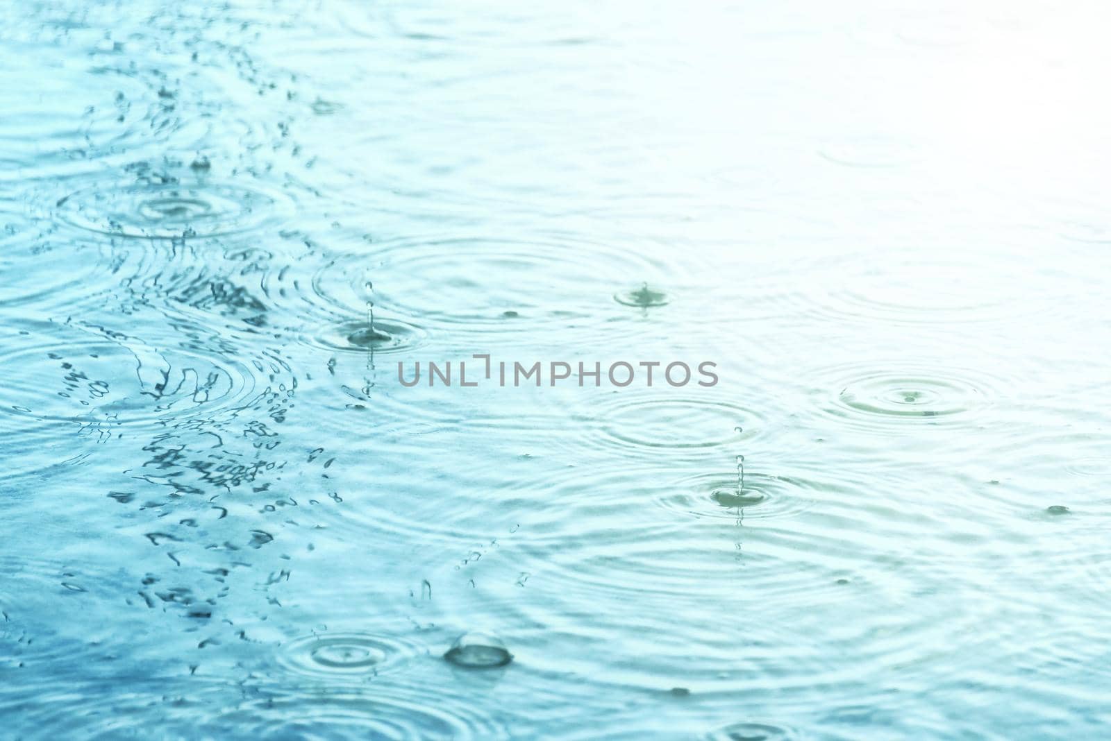 Raindrops creating concentric circles and droplets on water surface by dutourdumonde