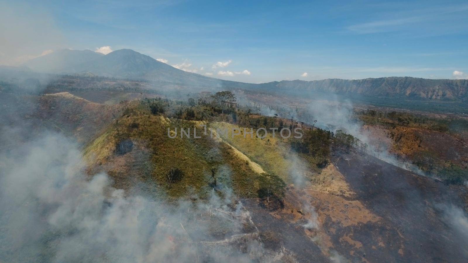 Aerial view forest fire on the slopes of hills and mountains. Forest and tropical jungle deforestation for human food farming and export. large flames from forest fire. Using fire to destroy natural habitat and causing large scale environmental damage in Asia. Jawa island, Indonesia.