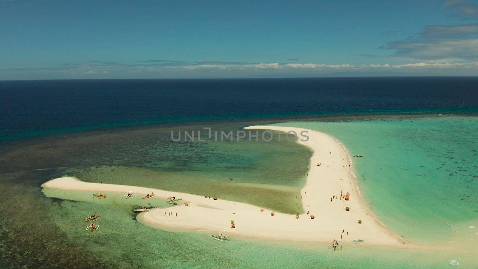 Tropical white island and sandy beach with tourists surrounded by coral reef and blue sea, aerial view. Sandbar Atoll. Island with sand bar and coral reef. Summer and travel vacation concept, Camiguin, Philippines.