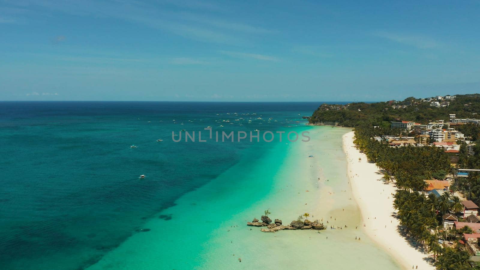 White Beach of Boracay and people swim at turquoise azure sea near Grotto Willy's Rock upon which stands the Virgin Mary Statue. Copy space for text. Summer and travel vacation concept.