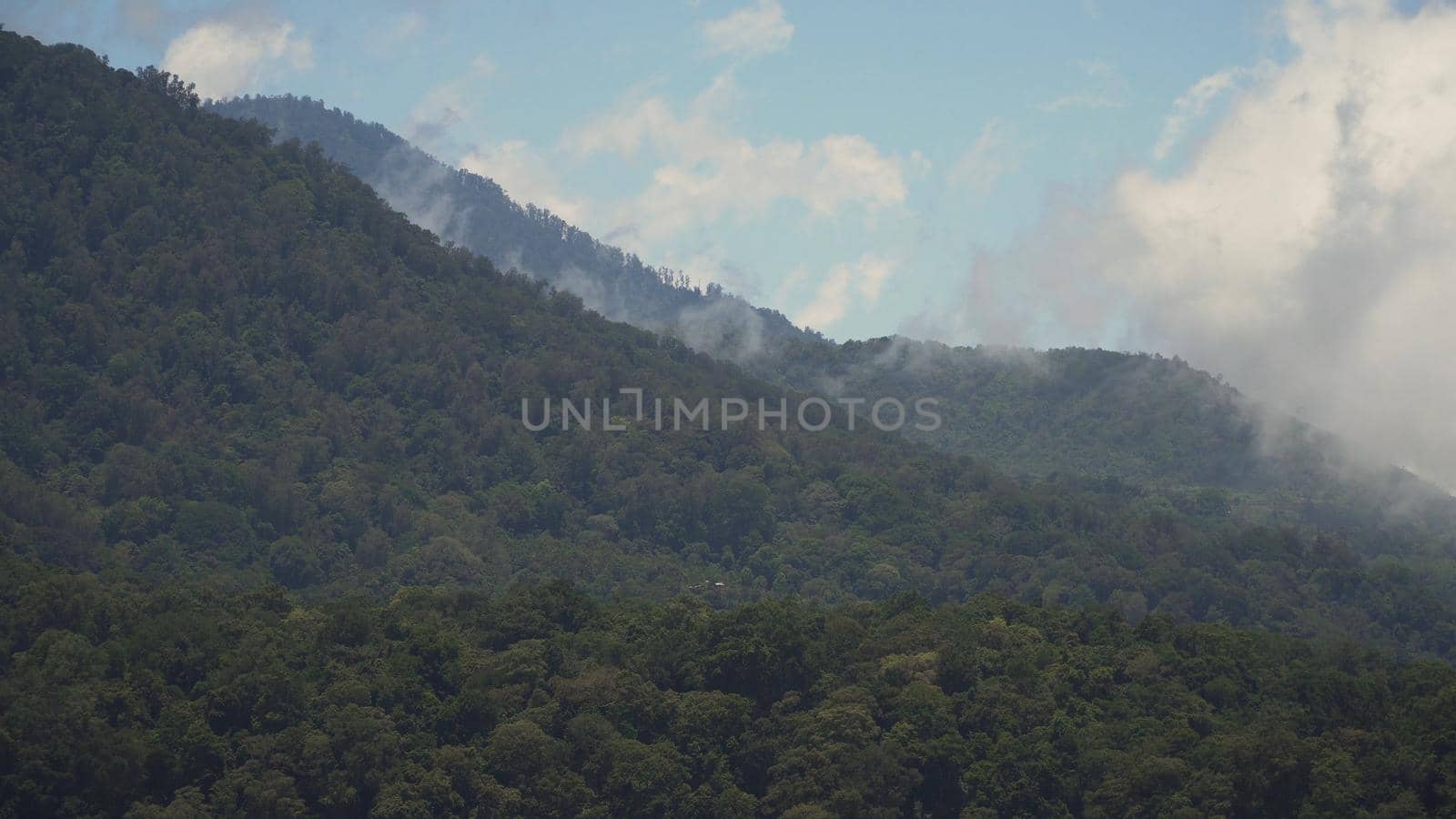 Tops of the mountains covered with forest in clouds and fog. Slopes of the mountains are covered with rainforest Bali, Indonesia. Mountain landscape, sky and clouds. Travel concept