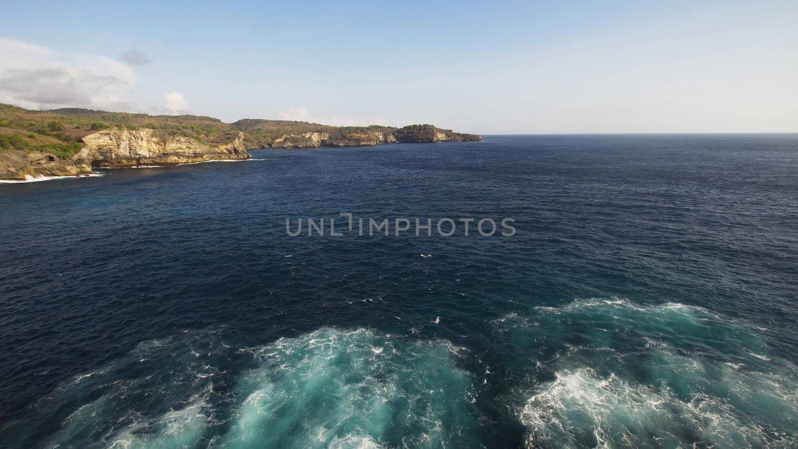 Rocky coast with high cliffs, sea surf with breaking waves on the coast, Nusa Penida, Indonesia. Ocean with waves and rocky cliff. Travel concept.