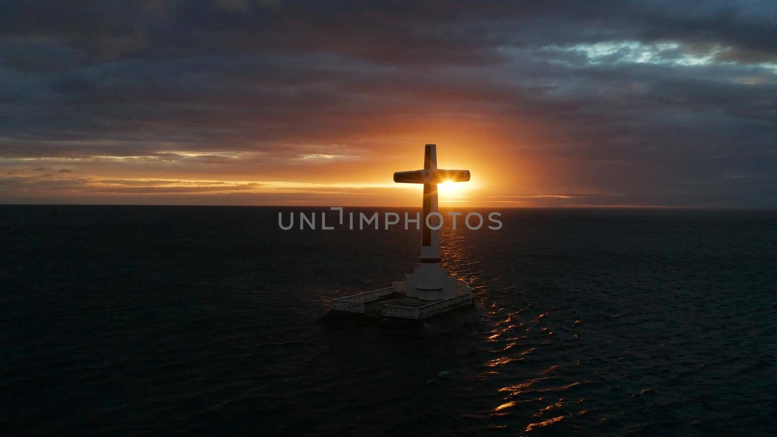 Catholic cross in sunken cemetery in the sea at sunset, aerial view. Colorful bright clouds during sunset over the sea. Sunset at Sunken Cemetery Camiguin Island Philippines.