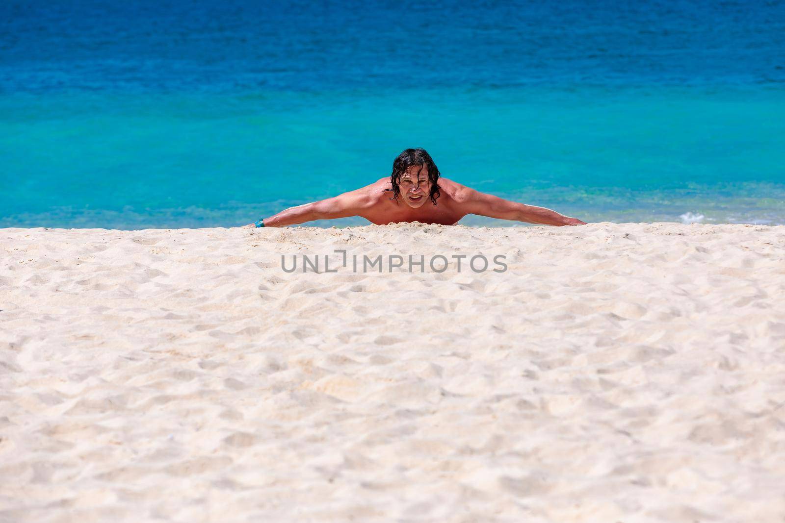 A man with long hair lies on the sand by the sea by Yurich32